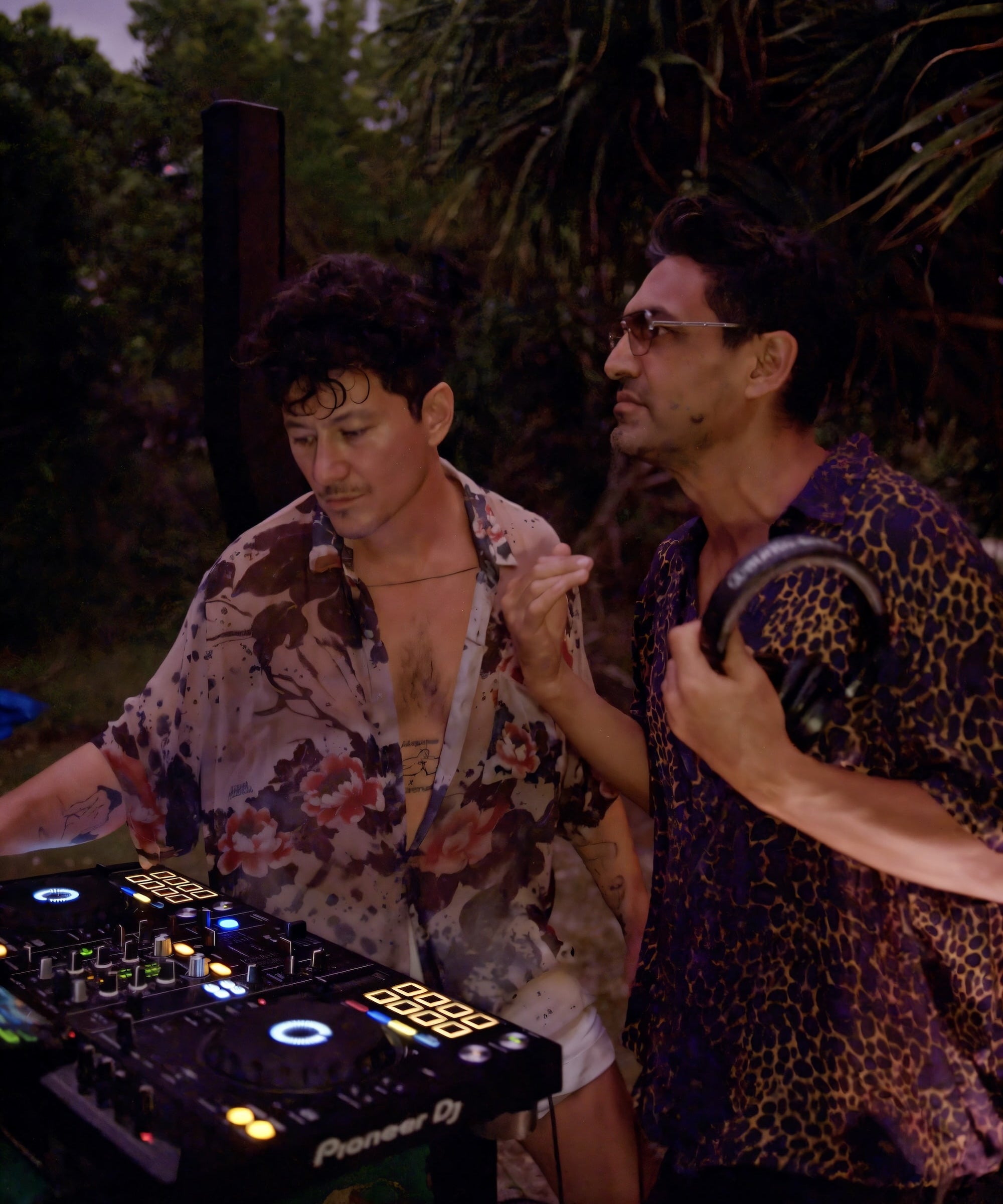 LEON DREAM standing next to a DJ mixer outdoors at night wearing LEON DREAM Apparel shirts.