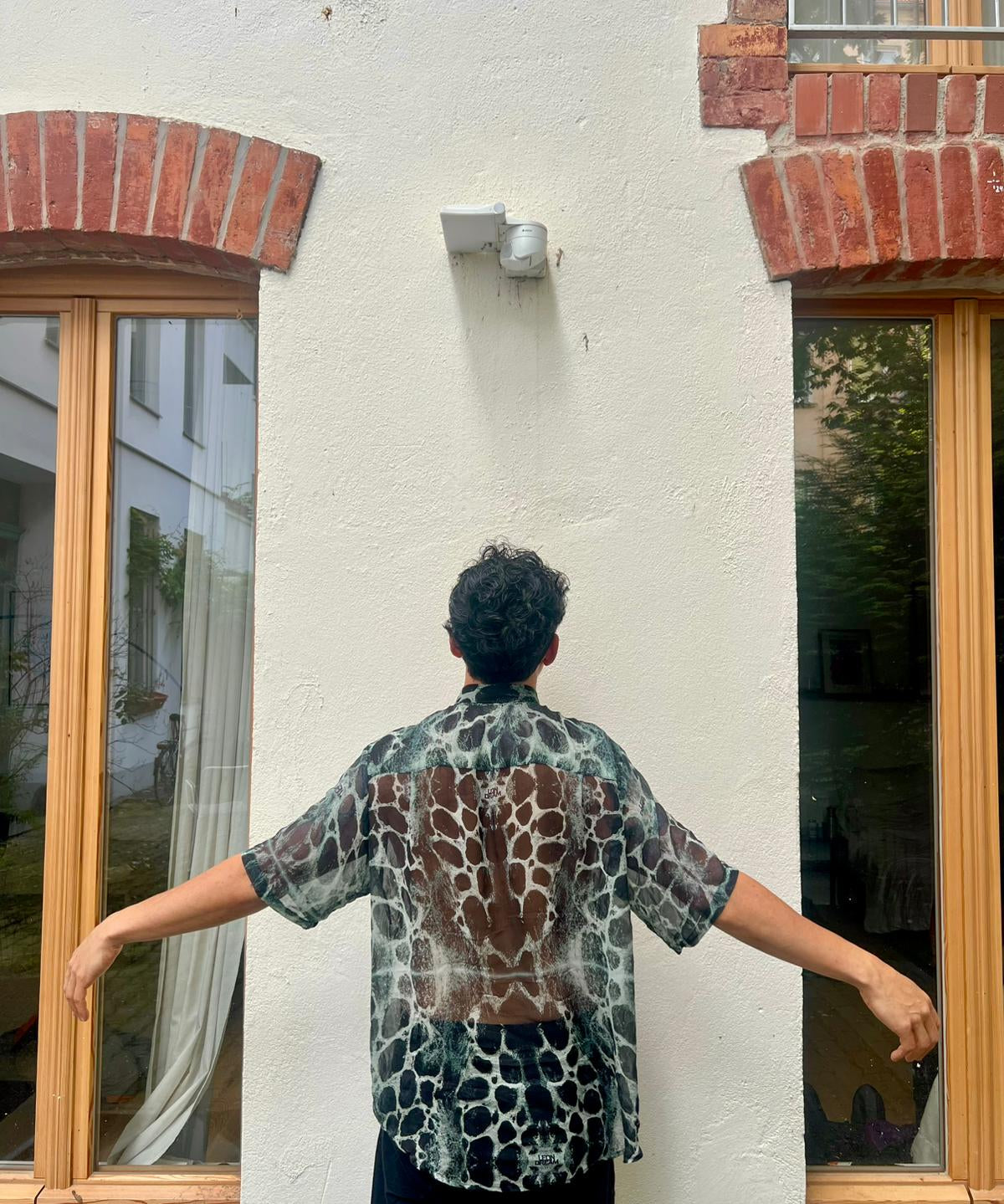 Person wearing a patterned Serengeti Stone silk shirt standing in front of a building.
