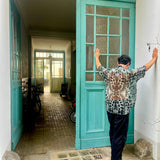 Model standing in front of a teal door with arms outstretched, while wearing Serengeti Stone shirt by Leon Dream.